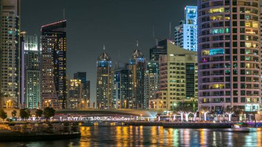 Dubai Marina rıhtımı, yatları ve Dubai 'deki köprüden modern kuleleri olan gece zaman çizelgesi, Birleşik Arap Emirlikleri. Bayraklı köprü