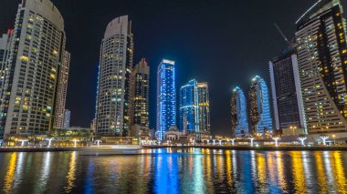 Dubai Marina gezinti güvertesinde yatlar ve modern kuleler Dubai 'deki deniz kıyısından yansıyan su, Birleşik Arap Emirlikleri' nin gece hiperhızlandırması. Yapay kanalla aydınlatılmış bölge