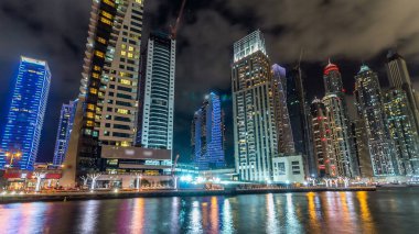 Dubai Marina güvertesi, deniz kenarındaki Birleşik Arap Emirlikleri gecesinden kalma yatlar ve modern kulelerle doludur. Çevresinde yapay kanallar ve aydınlık gökdelenler olan bir bölge.