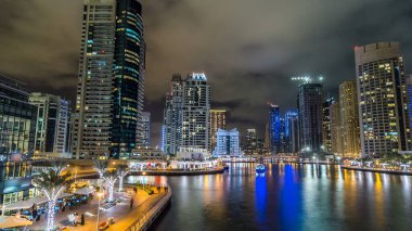 Dubai Marina gezinti güvertesinde yatlar ve modern kuleler ile deniz kenarındaki hiperhızlandırılmış sudan yansıtılır, Birleşik Arap Emirlikleri. Çevresinde yapay kanallar ve aydınlık gökdelenler olan bir bölge.