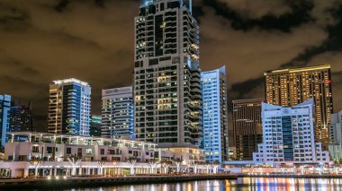 Dubai Marina kanalı üzerinde tekne ve köprüler, Dubai 'deki deniz kıyısından gece vakti yansıyan palmiyeler ve modern kuleler, Birleşik Arap Emirlikleri. Aydınlatılmış gökdelenler