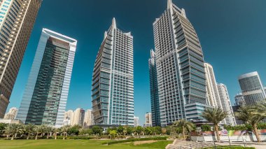 Rıhtımdaki palmiyeli gökdelenlerin hızlandırılmış görüntüsü. Dubai, BAE 'deki parkın yakınındaki Jumeirah Gölü Kuleleri' nde camla kaplı konut binaları. Parktan görüntüle
