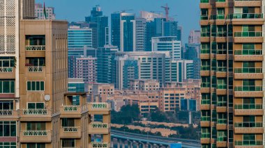 Golf sahasında gündüz vakti Şeyh Zized yolunda trafik varken. Golf sahasının yeşil çimenleri arka planda şehrin gökdelenleri gün batımında. Yan taraftaki modern kuleler