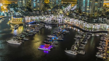 Dubai Marina gezinti güvertesi ve kanalı, Dubai, BAE 'de yüzen yat ve teknelerle dolu. Işıklı çeşme yanıp sönen ışıklar ve yol manzaralı trafik.