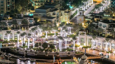 Yat limanında yüzen yatlar ve gece vakti teknelerle gezinen çeşme ve palmiyelerin manzarası. Dubai, BAE