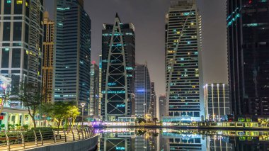 Rıhtımdaki aydınlık gökdelenlere palmiyeli gece görüşü. Dubai, BAE 'deki Jumeirah Gölü Kuleleri' ndeki konut binaları. Rıhtımdan görüntüle