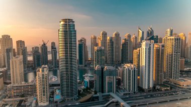 Dubai Marina ve Dubai, BAE 'deki JLT gökdelenlerinin günbatımı zaman çizelgesinde. Modern kuleler ve Şeyh zayed yolundaki trafik yukarıdan metro ve tramvay istasyonlarıyla