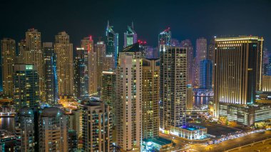Dubai Marina gezinti güvertesi ve kanalı, Dubai, BAE 'de yüzen yat ve teknelerle dolu. Yanıp sönen ışıkları ve yol trafiği olan aydınlık modern kuleler.