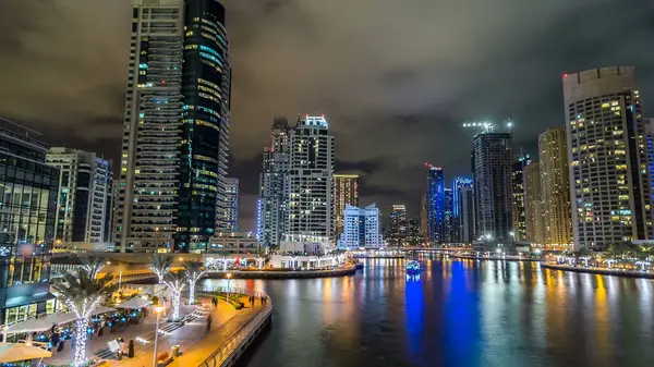 Dubai Marina gezinti güvertesinde yatlar ve modern kuleler ile deniz kenarındaki hiperhızlandırılmış sudan yansıtılır, Birleşik Arap Emirlikleri. Çevresinde yapay kanallar ve aydınlık gökdelenler olan bir bölge.