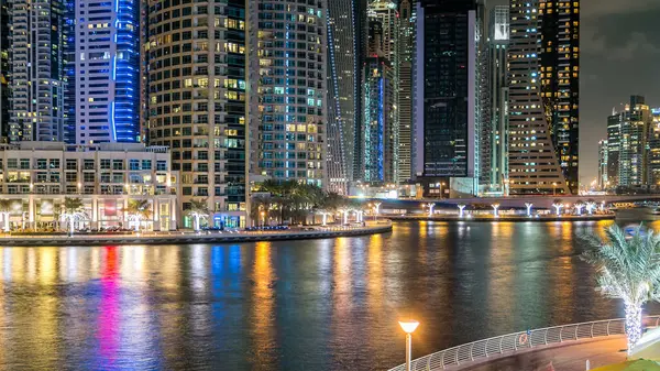 Dubai Marina 'da, Dubai gecesi, Birleşik Arap Emirlikleri' nin rıhtımından suya yansıyan tekneler, palmiyeler ve modern kuleler yer almaktadır. Gökdelende yapay kanalı ve aydınlatılmış pencereleri olan bir bölge