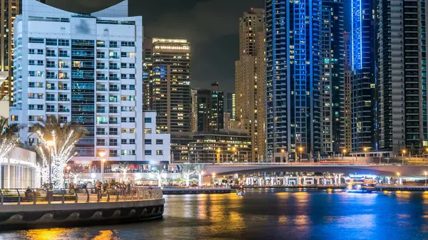 Dubai Marina 'da, Dubai gecesi, Birleşik Arap Emirlikleri' nin rıhtımından suya yansıyan tekneler, palmiye ve modern kuleler yer almaktadır. Gökdelenlerde suni kanalı ve aydınlatılmış pencereleri olan bir bölge