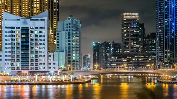 Dubai Marina 'da tekneler, palmiyeler ve modern kule Dubai' deki deniz kıyısından yansıyan su, Birleşik Arap Emirlikleri. Gökdelenlerde suni kanalı ve aydınlatılmış pencereleri olan bir bölge