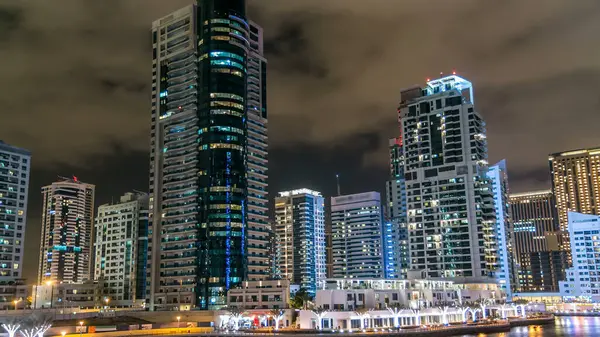 Dubai Marina 'da, Dubai gecesi, Birleşik Arap Emirlikleri' nin rıhtımından suya yansıyan tekneler, palmiyeler ve modern kuleler yer almaktadır. Gökdelende yapay kanalı ve aydınlatılmış pencereleri olan bir bölge