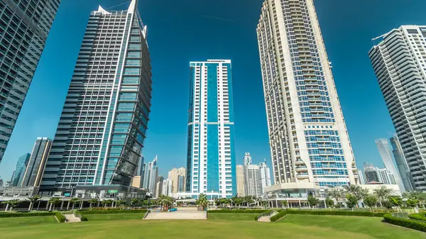 Rıhtımdaki palmiyeli gökdelenlerin hızlandırılmış görüntüsü. Dubai, BAE 'deki parkın yakınındaki Jumeirah Gölü Kuleleri' nde camla kaplı konut binaları. Parktan görüntüle