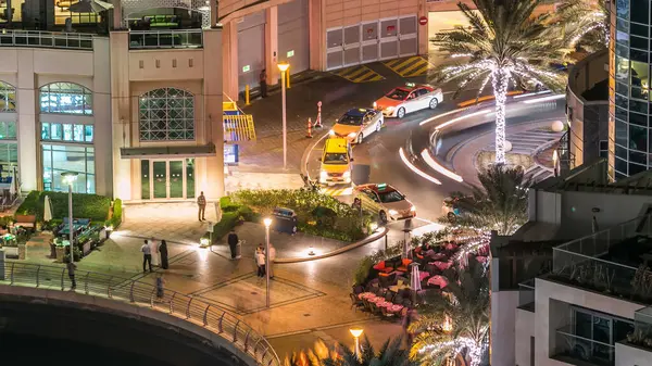 Dubai Marina 'nın gece hava manzarası. Restoranları, yüzen yatları ve botları olan kanalları var. Aydınlatılmış modern kuleler. Işıkları ve trafiği daire şeklindeki yolda taksi parkı olan.