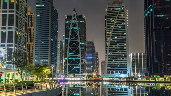 Rıhtımdaki aydınlık gökdelenlere palmiyeli gece görüşü. Dubai, BAE 'deki Jumeirah Gölü Kuleleri' ndeki konut binaları. Rıhtımdan görüntüle