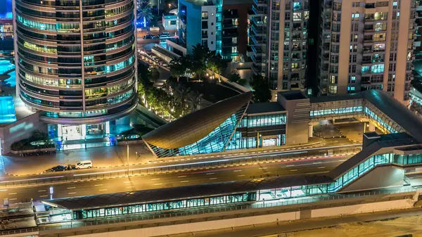 Metro ve tramvay istasyonu. Dubai Marina gezinti güvertesi ve kanalı, Dubai, BAE 'de yüzen yat ve tekneleri olan hava manzaralı. Yanıp sönen ışıkları ve yol trafiği olan aydınlık modern kuleler