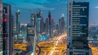 Dubai şehir mimarisi günden geceye geçiş zamanı. Şeyh Zayed yolu üzerindeki gökdelenler aydınlanmış ve kavşakta trafik var. Güzel bulutlu gökyüzü