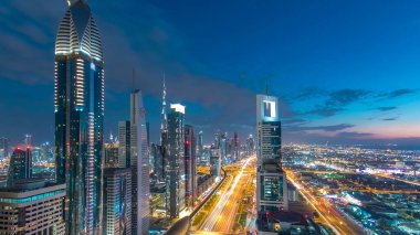 Dubai şehir mimarisi günden geceye geçiş zamanı. Şeyh Zayed yolu üzerindeki aydınlık gökdelenler ve trafik manzaralı üst hava manzarası. Güzel bulutlu gökyüzü
