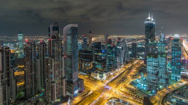 Dubai iş hangarı kuleleri gece vakti aydınlatılıyor. Kavşakta trafik vardı. Bazı gökdelenlerin çatısı ve inşaat halindeki yeni kulelerin havadan görüntüsü.