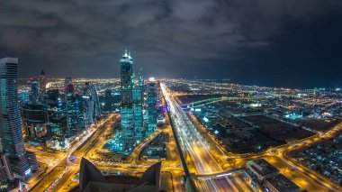 Dubai iş hangarı kuleleri gece aydınlandı. Dubai su kanalı, köprüler ve Şeyh Zayed yolu trafiği. Bazı gökdelenlerin çatı manzarası ve inşaat halindeki yeni kuleler. Bulutlu gökyüzü