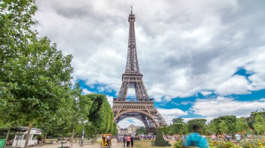 Champ de Mars ve Eyfel Kulesi güneşli bir yaz gününde hızlandırılmış zaman atlaması. Paris, Fransa. Yeşil ağaçlar ve bulutlu gökyüzü, etrafta yürüyen insanlar. Önerge