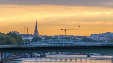 Paris 'te şafak söktükten sonra, tren yolu köprüsü (Pont Rouelle) adayı (Ile des Cygnes) geçmektedir. Turuncu gökyüzü ve Seine nehrinin suları üzerinde yansıması. İnşaat alanı vinçleri