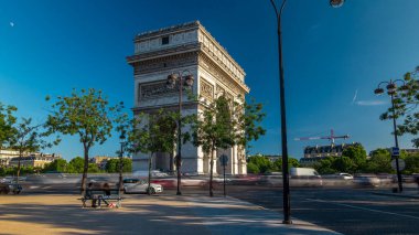 Arc de Triomphe zaman atlaması. Çevrede trafik ve ağaçlar var. Paris 'teki ünlü anıt Şanzelize' nin batı ucunda duruyor. Yazın mavi bulutlu gökyüzü