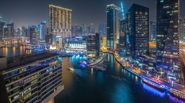 Dubai Marina 'daki su kanalı gece vakti panoramik ufuk çizgisi. Işıklı ve aydınlatmalı kuleler. Gökdelenlerin yakınında trafik olan yüzen yatlar ve tekneler.