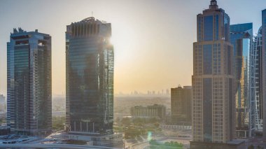 Jumeirah göl kulelerinin gündoğumunda gökdelenlerin havadan görünüşü cam yüzeyden yansıyan güneşle birlikte. Dubai marinasından çatı manzarası