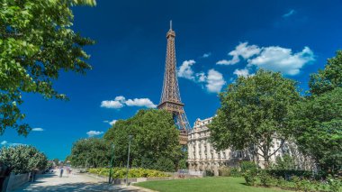 Eiffel Kulesi, Paris 'teki Siene nehri kıyılarından gösterildi. Zaman ayarlı hiperhız, Fransa. Yazın mavi bulutlu gökyüzü Yeşil ağaçlar ve etrafta yürüyen insanlar