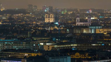Paris 'te bir gece vakti çatıların üstündeki hava manzarası. Aydınlatılmış Notre Dame de Paris ve Saint-Sulpice katedrali manzaralı. Işıklar kapanıyor.