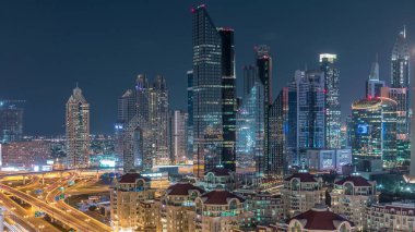 Dubai gece timelapse ışıklı gökdelenler ve yol kavşağı havadan görünümü. Etrafında modern kuleleri ile şehir merkezinde kavşakta Trafik. Bulutlu gökyüzü