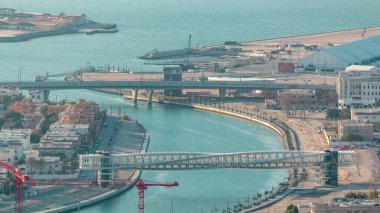 Downtown gökdelenler çatıdan gün batımı hava timelapse sırasında yaya köprüsü ile Dubai su kanalı. Yüzer tekneler ve vinçli şantiye