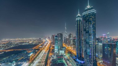 Dubai, Bae'de şeyh zayed yol gece timelapse modern gökdelenler ve trafik ile Akşam silueti. Işıklı iş koyu mimarisinin havadan görünümü.