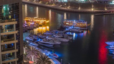 Dubai Marina körfezindeki iskeleye park etmiş lüks yatlar. Şehir hava manzaralı gece manzaralı. Etrafında kuleler ve gökdelenler olan gezinti yolu