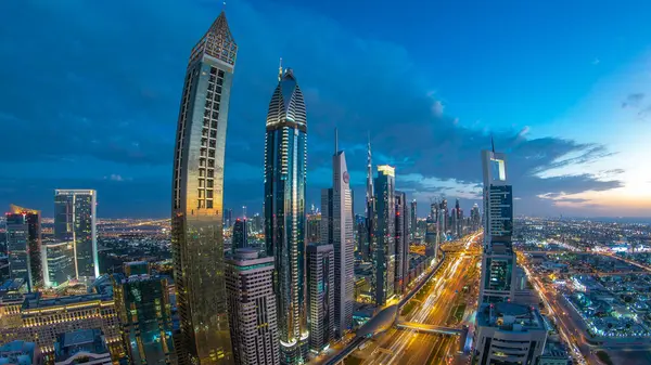 Dubai şehir mimarisi günden geceye geçiş zamanı. Şeyh Zayed yolu üzerindeki aydınlık gökdelenler ve trafik manzaralı üst hava manzarası. Güzel bulutlu gökyüzü. Fisheye merceği
