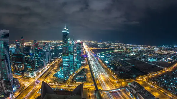Dubai iş hangarı kuleleri gece aydınlandı. Dubai su kanalı, köprüler ve Şeyh Zayed yolu trafiği. Bazı gökdelenlerin çatı manzarası ve inşaat halindeki yeni kuleler. Bulutlu gökyüzü