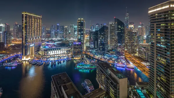 Dubai Marina hava saatinin gece aydınlanması, BAE. Modern gökdelenler ve konut binaları. Yollarda trafik vardı. Yapay kanal şehrindeki alışveriş merkezinin yakınındaki yatlar ve tekneler.