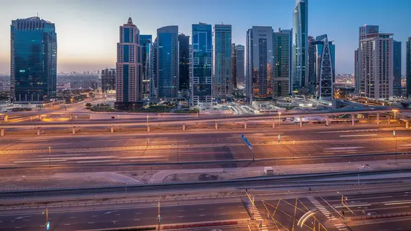 Jumeirah lakes hava görünümünü gün geçiş timelapse Şeyh zayed road ve metro hattı üzerinde trafik ile gecesine ışıklandırılmış gökdelenler ile kuleleri. Dubai Yat Limanı güneş doğmadan önce çatı görünümü