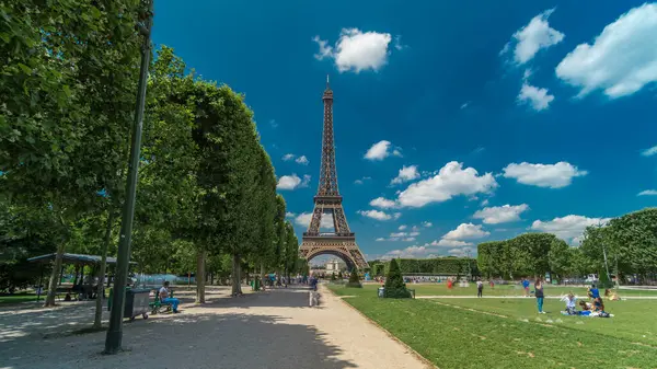 Paris 'teki Champs de Mars' taki Eyfel Kulesi. Zaman atlaması, Fransa. Yazın mavi bulutlu gökyüzü Ağaçlı yeşil çimenler ve etrafta yürüyen insanlar.