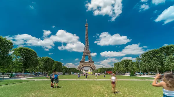 Paris 'teki Champs de Mars' taki Eyfel Kulesi. Zaman atlaması, Fransa. Yazın mavi bulutlu gökyüzü yeşil çimlerle kaplı ve insanlar etrafta dolaşıyor. İlerliyorum.