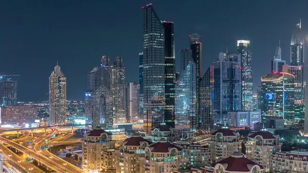 Dubai gece timelapse ışıklı gökdelenler ve yol kavşağı havadan görünümü. Etrafında modern kuleleri ile şehir merkezinde kavşakta Trafik. Bulutlu gökyüzü