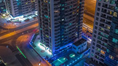 Dubai Marina 'daki yüzme havuzu ve kavşağındaki gökdelenlerin görüntüsü. Kentsel ufuk çizgisinde aydınlatılmış modern binalar