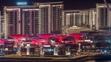 Dubai'deki Bluewaters Adası'nda ışıklı binalarla gece saati. Yatlar ve tekneler geçiyor. Jumeirah Beach Residence kıyılarında bulunan insan yapımı ada