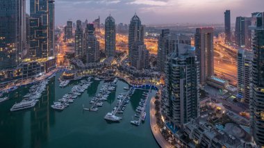 Dubai Marina gece gündüz geçiş timelapse havadan üst görünümü. Dubai, Bae gün doğumundan önce yüzen yatlar ve tekneler ile gezinti ve kanal. Işıklı modern kuleler ve yolda trafik