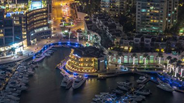 Dubai marina gece zaman atlamalı yüzen yatlar havadan görünümü. Yolda trafik var. Mağazalar ve restoranlar ile Aydınlatılmış gezinti.