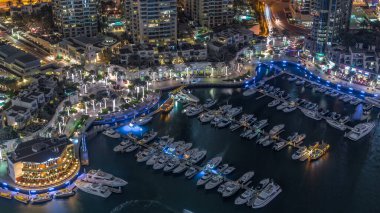 Dubai Marina Limanı 'nda gece vakti deniz kenarında modern yatlar var. Kanalda yüzen tekneler kuleleri ve gökdelenleri çevreledi..