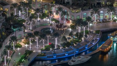 Dubai Marina Yürüyüşü 'nde fıskiye ve palmiyeli Top View gece zaman çizelgesi. Yat ve teknelerle aydınlatılmış rıhtım