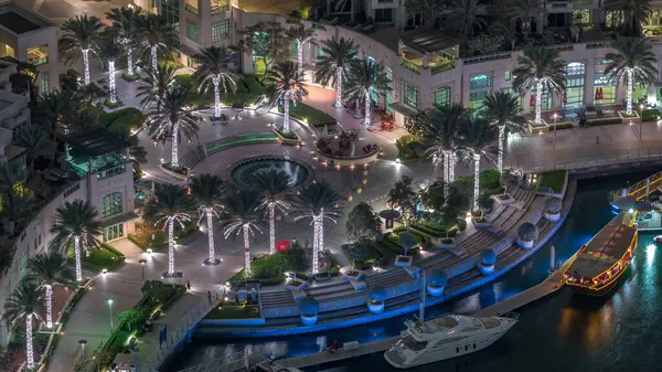 Dubai Marina Yürüyüşü 'nde fıskiye ve palmiyeli Top View gece zaman çizelgesi. Yat ve teknelerle aydınlatılmış rıhtım